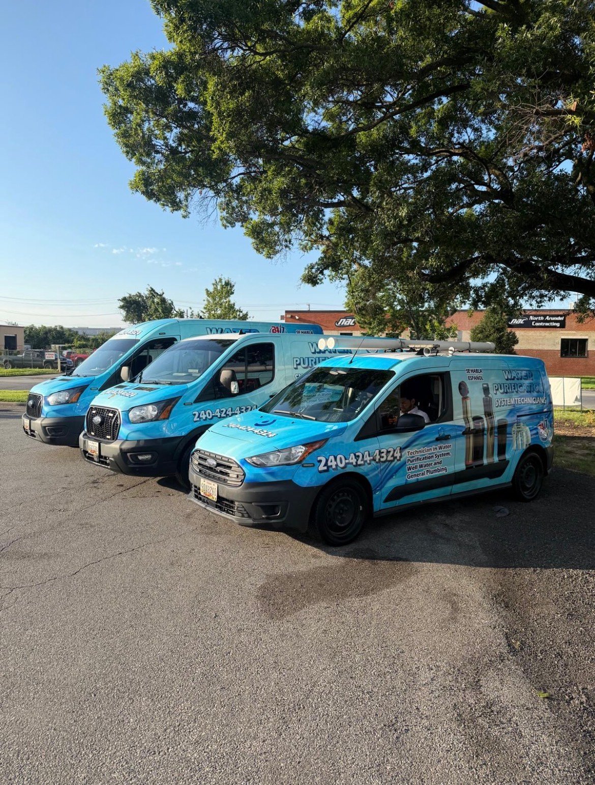 Three blue and white service vans parked in a row outside the Water Purification System Technicians shop.